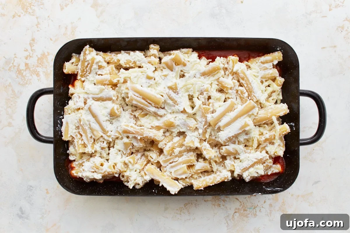 Comforting Gluten-Free Ziti Bake 11 black baking dish with cheese covered gluten-free pasta on top of a layer of marinara sauce
