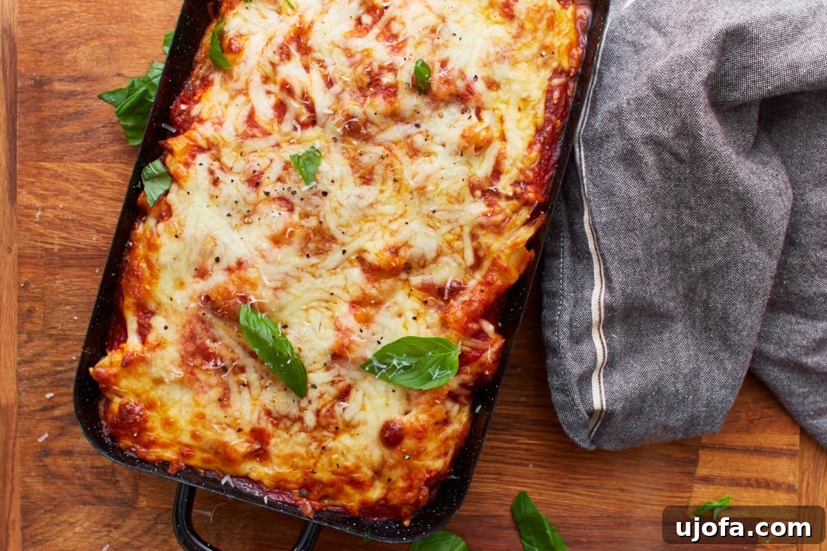 Comforting Gluten-Free Ziti Bake 15 overhead view of baked gluten-free baked ziti in black baking dish on wooden counter with gray rag next to it.