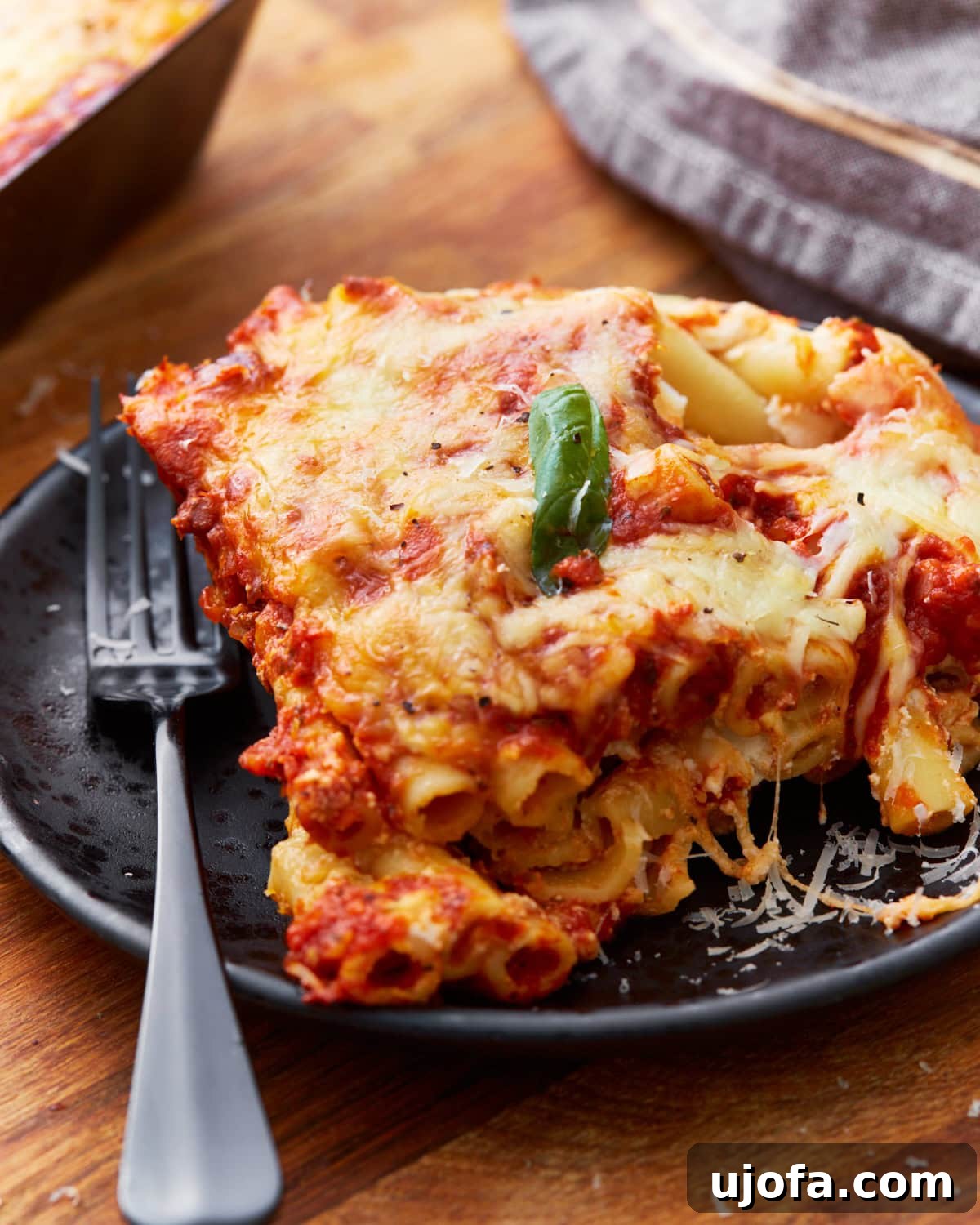 Comforting Gluten-Free Ziti Bake 5 front on view of gluten-free baked ziti on black plate with a leaf of fresh basil on top and a black fork