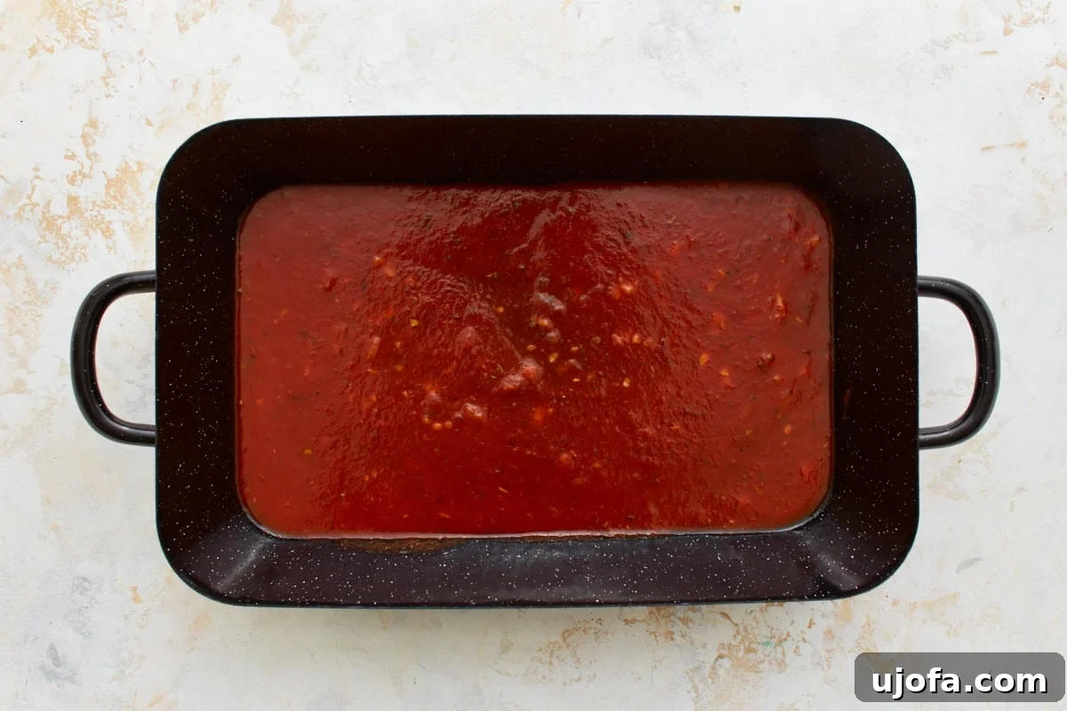 Comforting Gluten-Free Ziti Bake 9 black baking dish with marinara sauce spread on the bottom