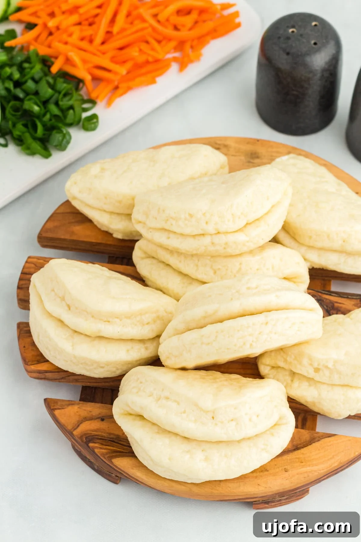 A stack of perfectly steamed, warm gluten-free bao buns on a round wooden cutting board, ready for delicious fillings.