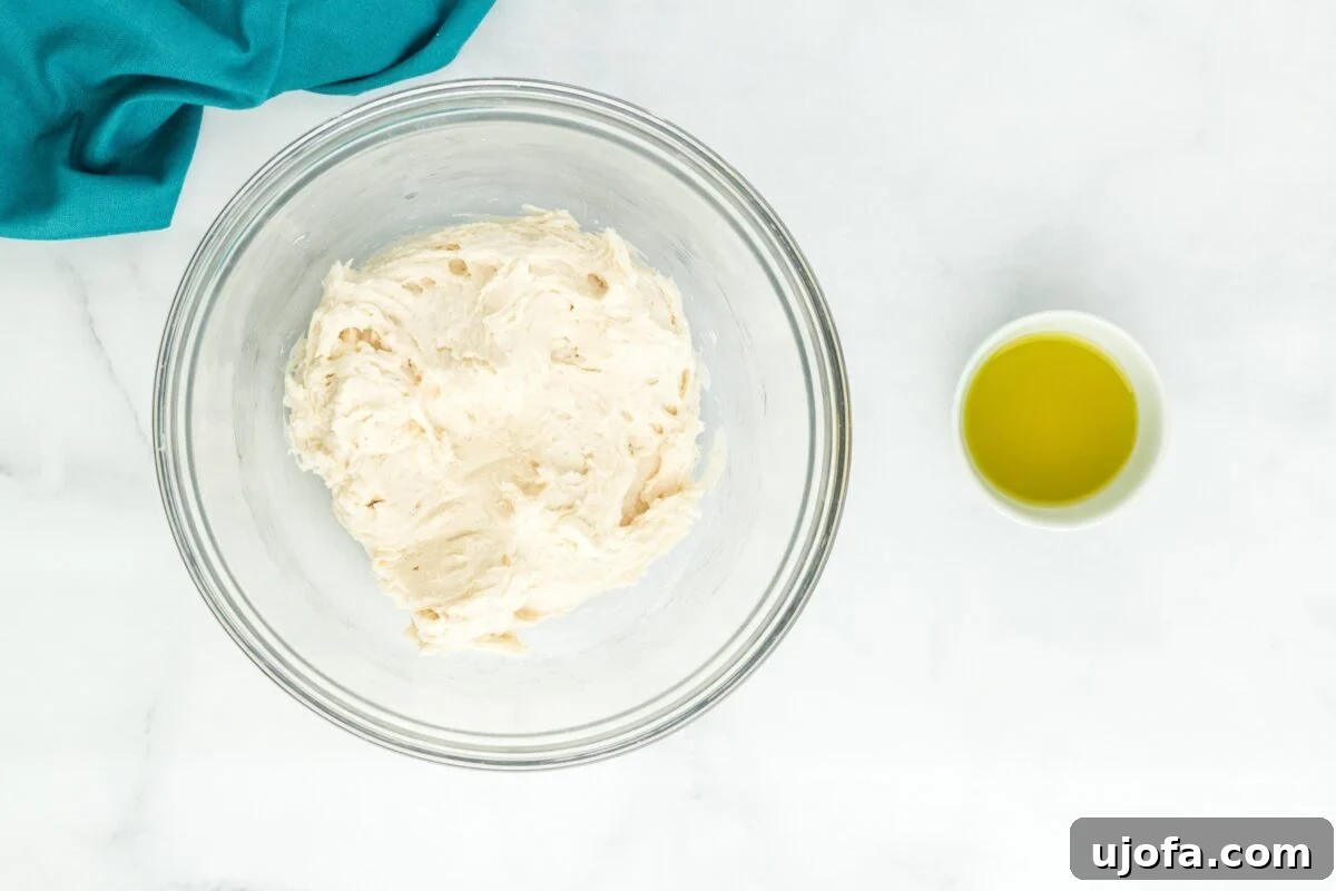 A freshly formed ball of gluten-free bao bun dough resting in a clear glass bowl, placed beside a small bowl of olive oil.