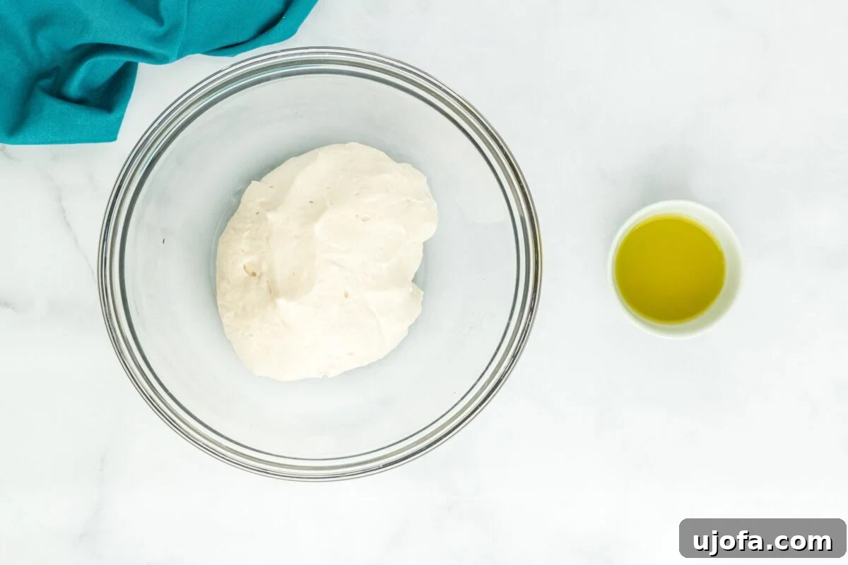 A ball of gluten-free bao bun dough, having risen and expanded, resting in a glass bowl covered with plastic wrap.