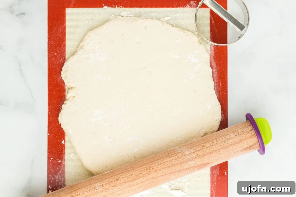 Rolled out gluten-free bao bun dough spread on a silicone mat, with a rolling pin nearby, ready for cutting.