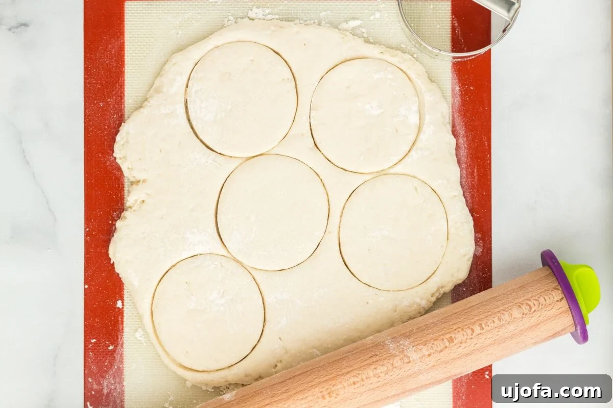 Five circles expertly cut from the rolled-out gluten-free bao bun dough, resting on a silicone mat with a rolling pin beside them.