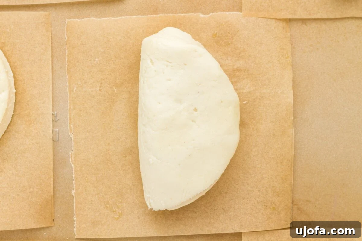 A perfectly folded, uncooked gluten-free bao bun, resting on its individual parchment paper square, awaiting steaming.