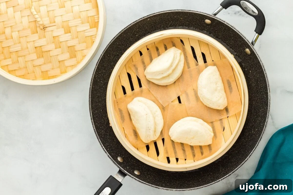 Four gluten-free bao buns arranged in a bamboo steamer basket, positioned inside a black skillet filled with water, ready for steaming.