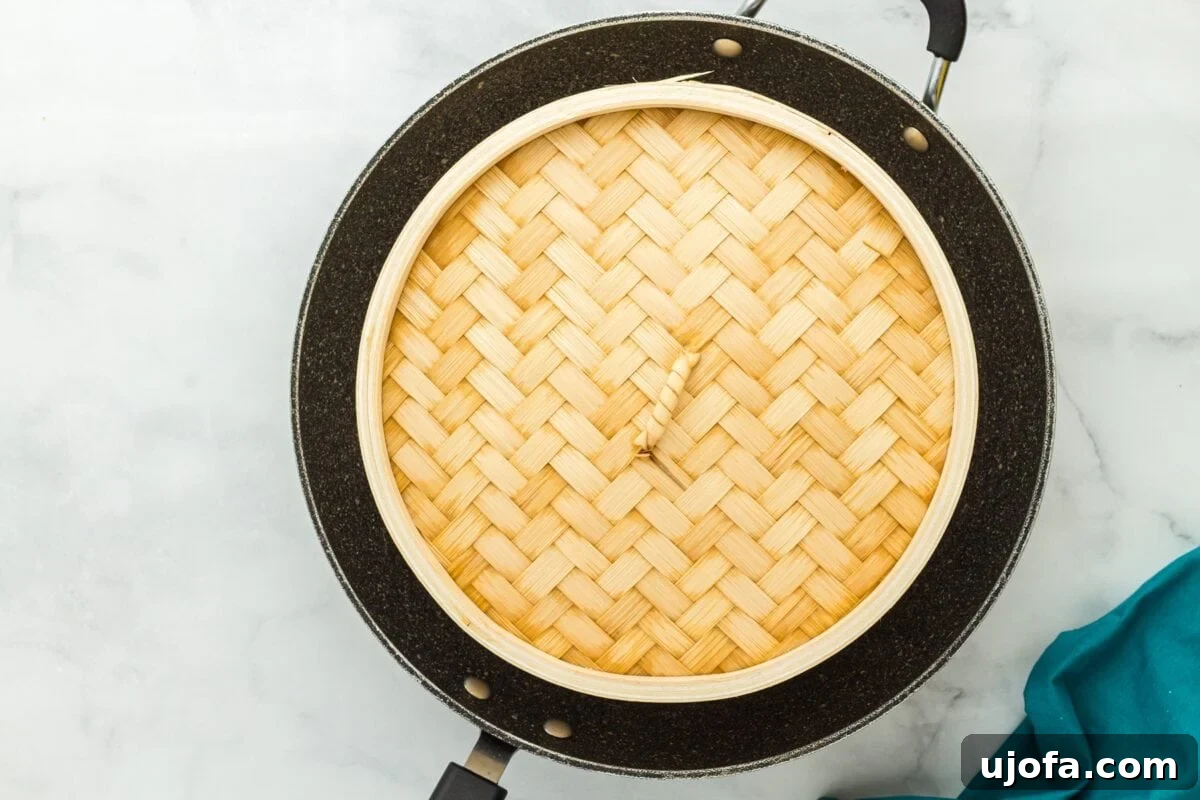A bamboo steamer basket with its lid securely in place, nestled inside a black skillet on a stovetop, as the gluten-free bao buns steam within.