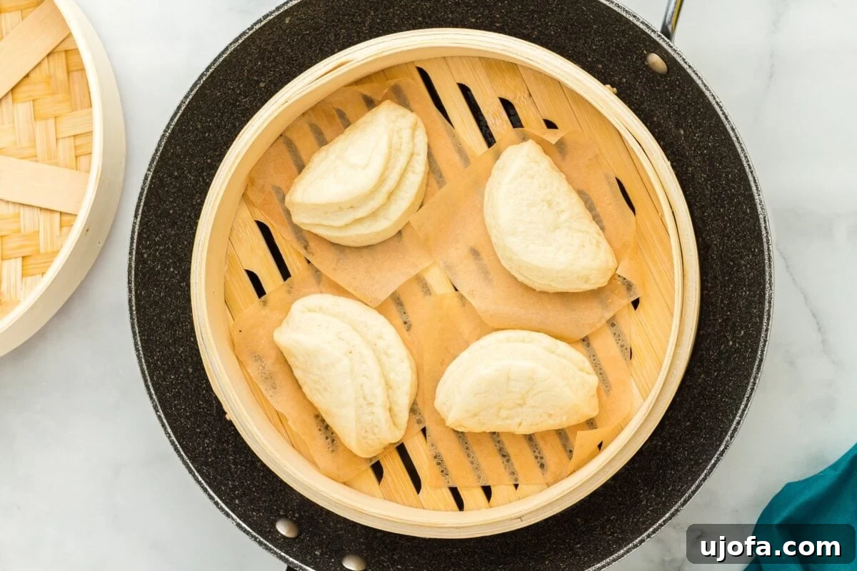 An uncovered bamboo steamer basket revealing four perfectly steamed gluten-free bao buns, fluffy and ready.