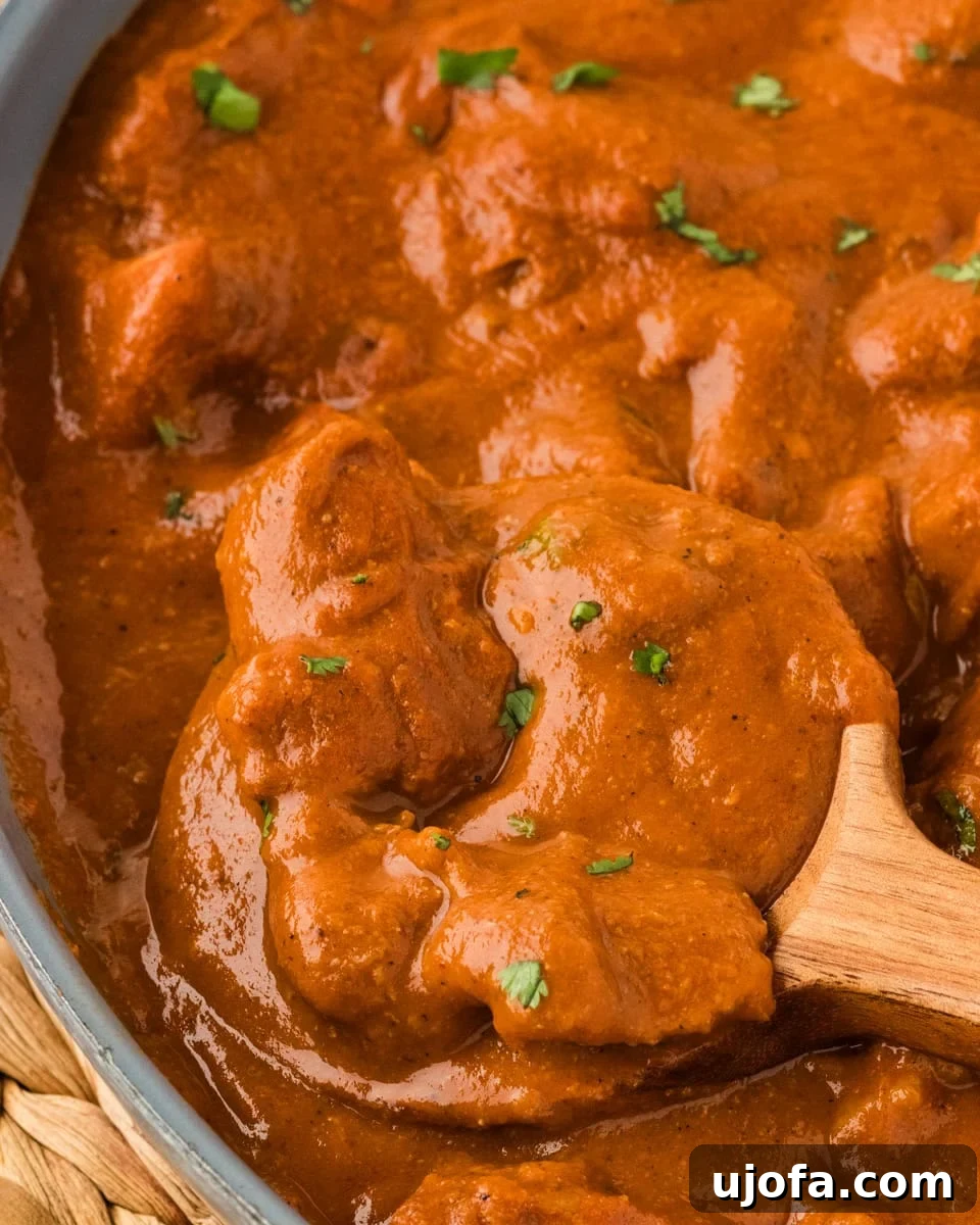 Close-up shot of the rich and creamy dairy-free butter chicken simmering in a skillet, with a wooden spoon stirring the sauce.