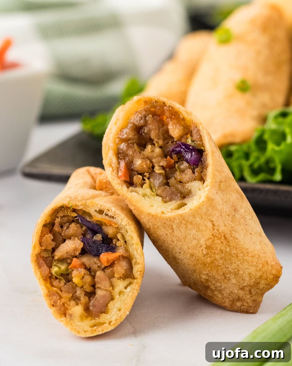 Guilt-Free Crispy Egg Rolls 2 Two golden-brown gluten-free egg rolls, sliced in half, resting on each other, showcasing their vibrant filling.