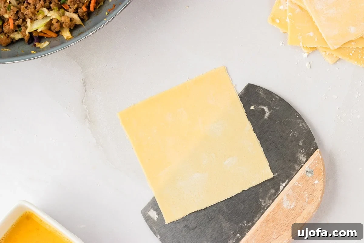 Guilt-Free Crispy Egg Rolls 19 A single 4-inch square of gluten-free egg roll dough being gently lifted with a dough cutter from a cornstarch-dusted surface.