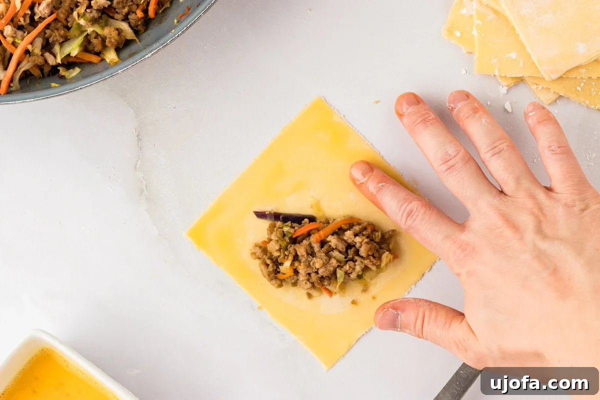 Guilt-Free Crispy Egg Rolls 22 A hand gently applying egg wash to the exposed edges of a gluten-free egg roll wrapper, ready for folding.