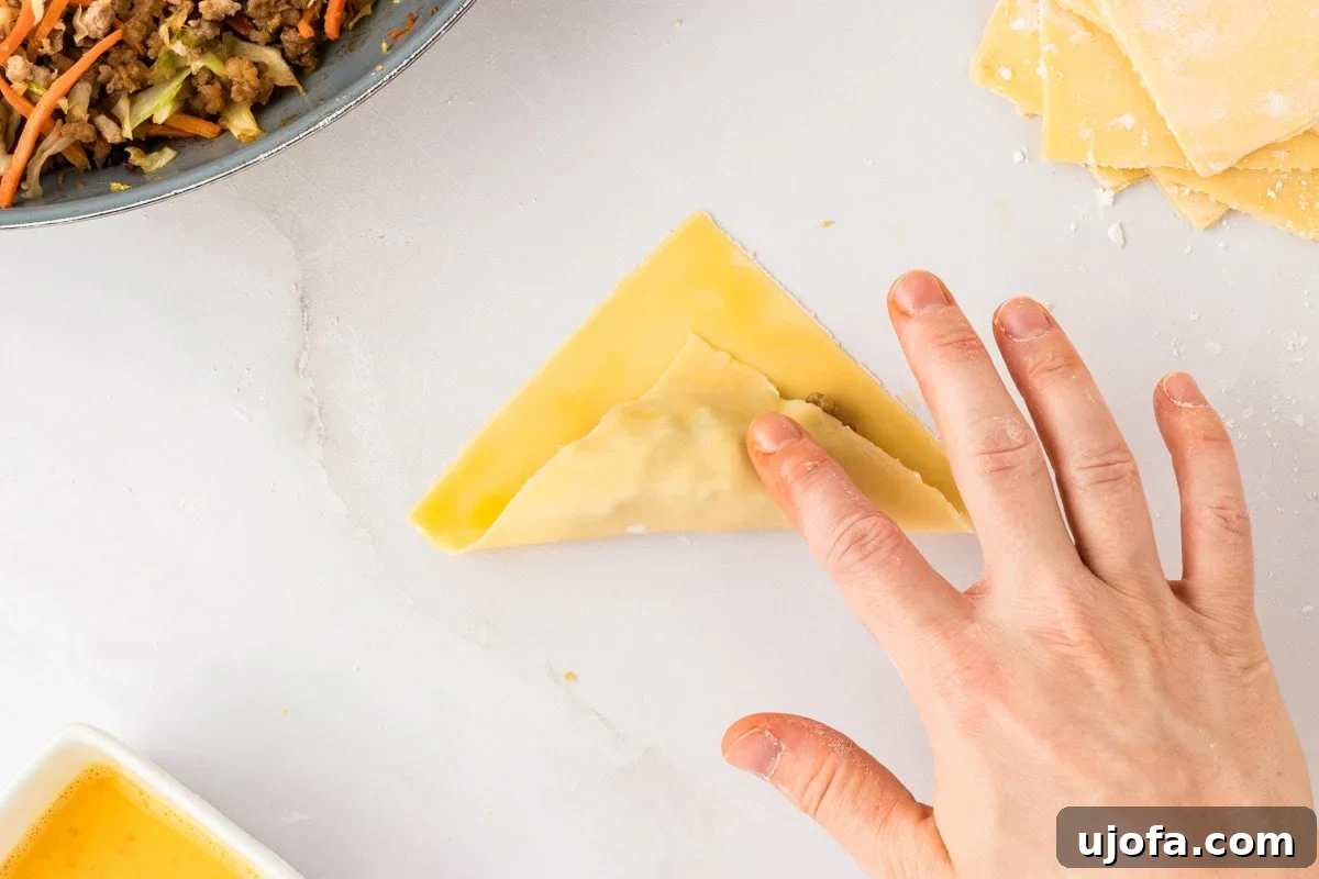 Guilt-Free Crispy Egg Rolls 23 The bottom corner of a gluten-free egg roll wrapper being carefully folded over the log of filling.