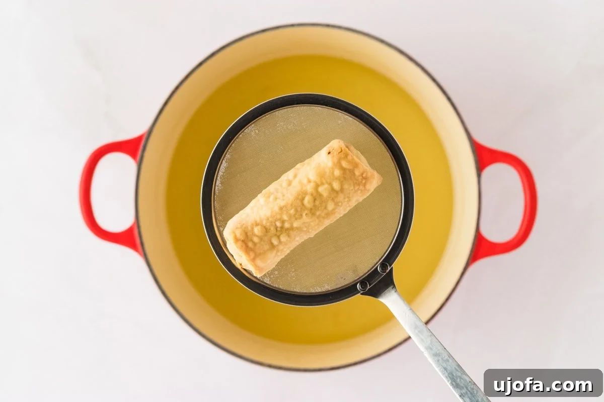 Guilt-Free Crispy Egg Rolls 26 A single golden-brown gluten-free egg roll being lifted from hot frying oil with a skimmer over a red pot.