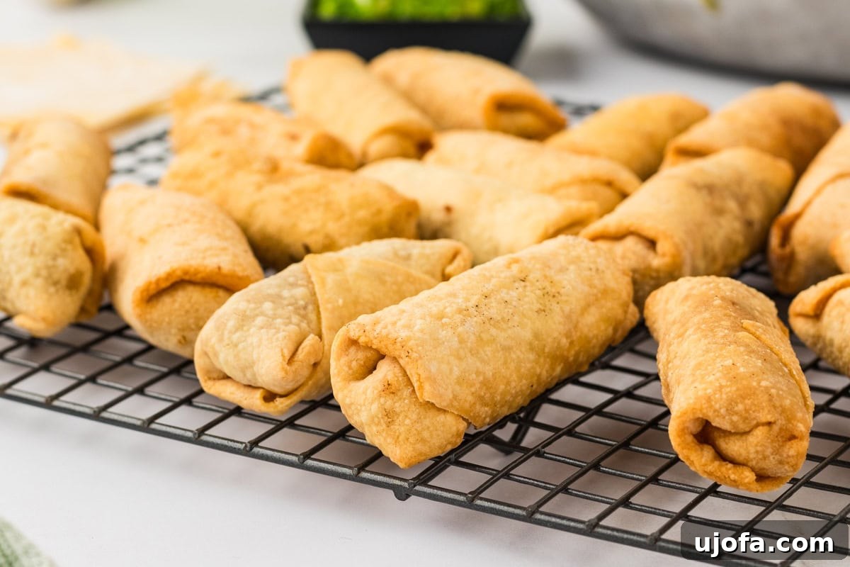 Guilt-Free Crispy Egg Rolls 27 A collection of freshly fried, golden-brown gluten-free egg rolls resting on a metal drying rack.
