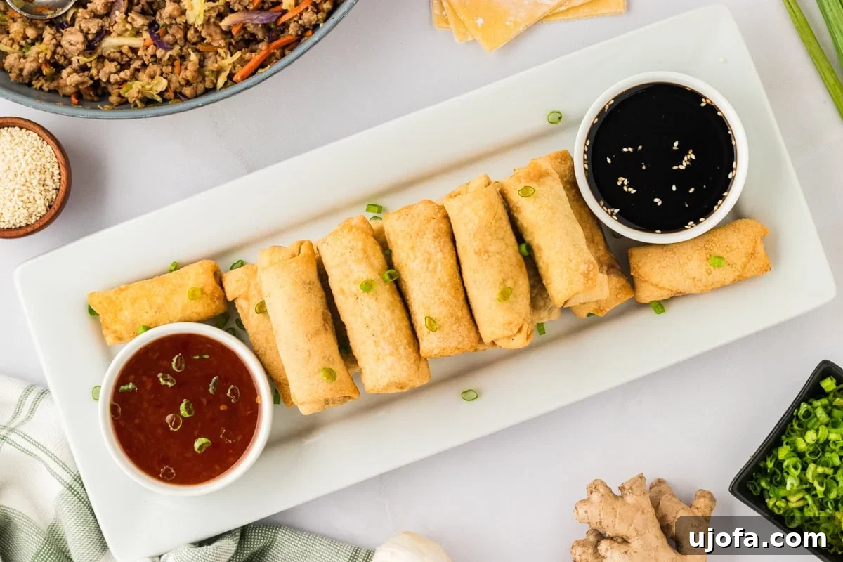 Guilt-Free Crispy Egg Rolls 28 A white rectangular plate laden with an abundance of fried gluten-free egg rolls, flanked by small white bowls of sweet chili sauce and gluten-free soy sauce.
