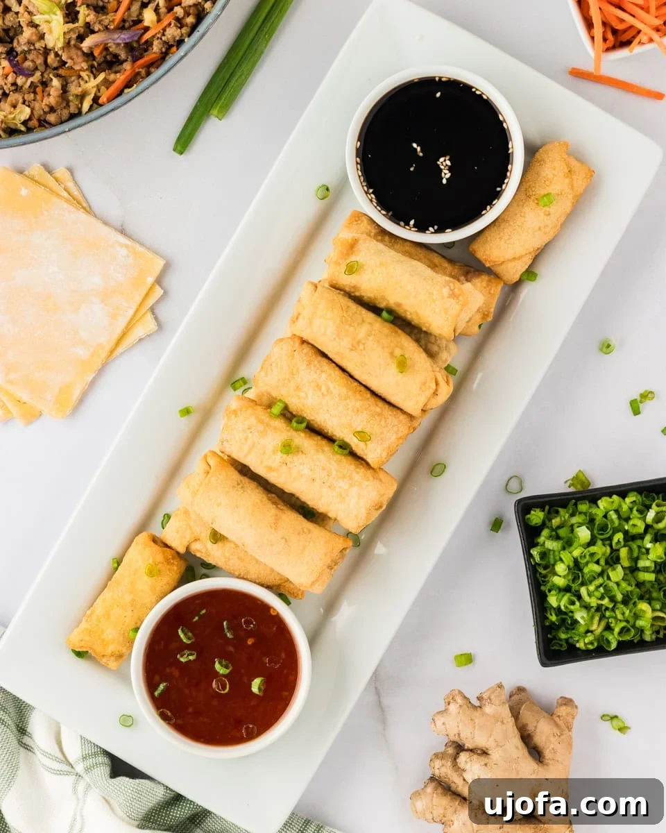 Guilt-Free Crispy Egg Rolls 4 A beautifully arranged plate of golden-brown gluten-free egg rolls, accompanied by small bowls of sweet chili sauce and gluten-free soy sauce for dipping.