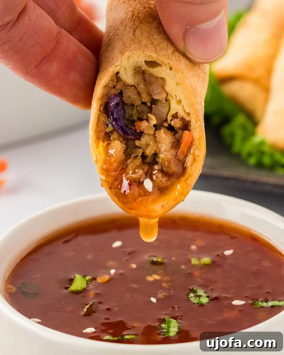 Guilt-Free Crispy Egg Rolls 5 A golden-brown gluten-free egg roll being dipped into a bowl of vibrant sweet chili sauce.