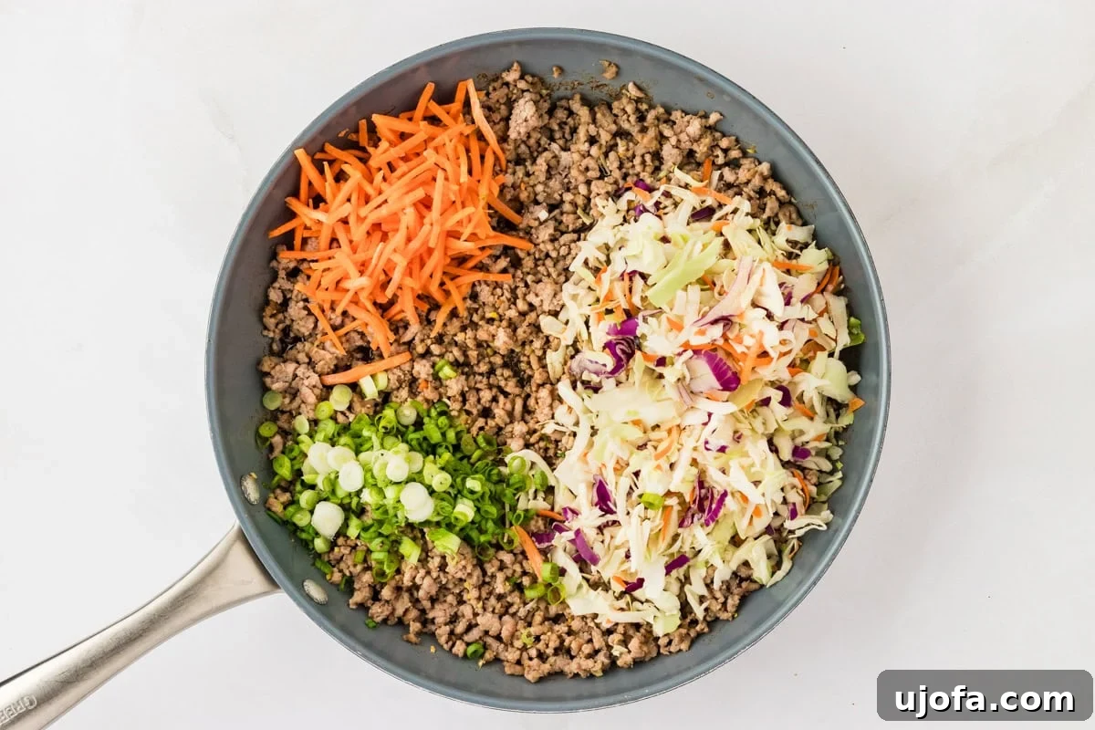 Guilt-Free Crispy Egg Rolls 9 Cooked ground pork in a skillet, topped with a colorful mix of coleslaw, shredded carrots, and sliced green onions, ready for the sauce.