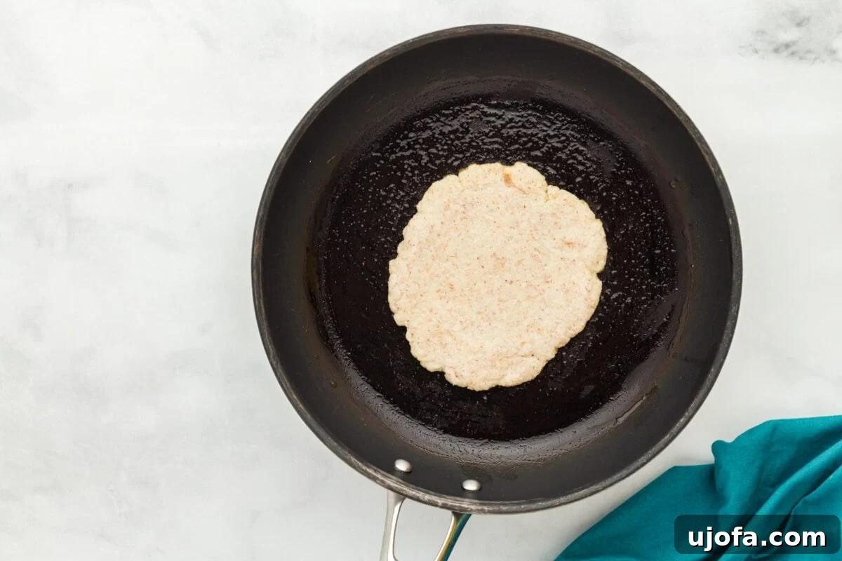An uncooked coconut flour tortilla placed in a black skillet greased with olive oil, ready for cooking.