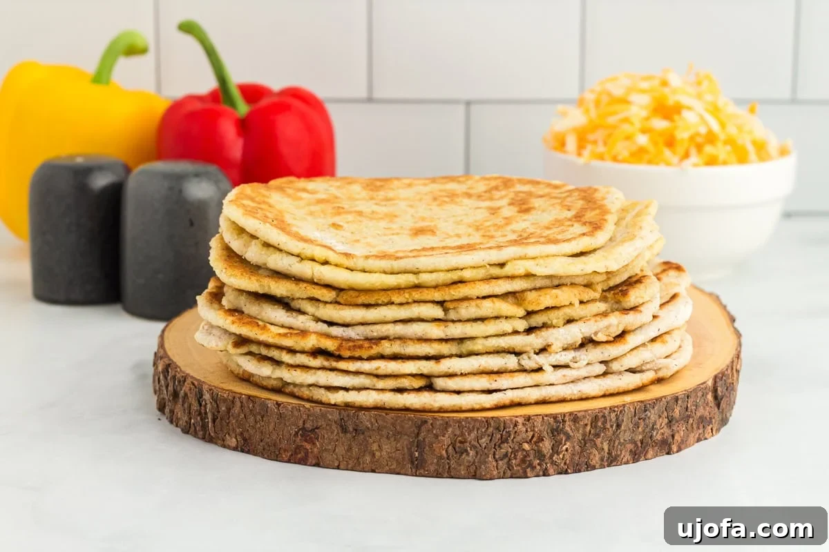 A stack of freshly cooked coconut flour tortillas on a wooden board, with colorful bell peppers and shredded cheese in the background, inviting a delicious meal.