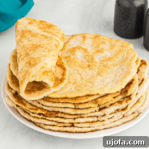 One coconut flour tortilla rolled up and stacked on other tortillas on a white plate, showcasing the soft texture.
