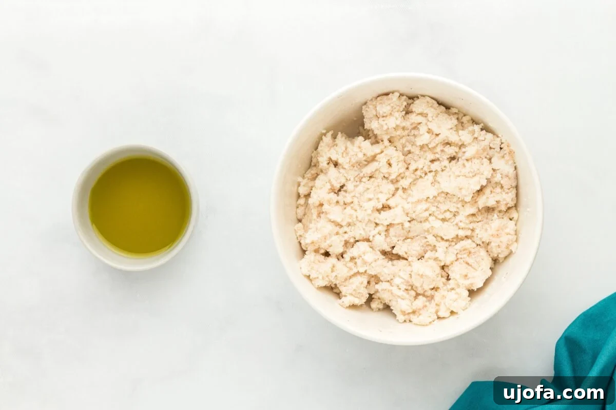 A white bowl filled with dry ingredients like coconut flour, psyllium husk, baking powder, onion powder, garlic powder, and salt, next to a small bowl of olive oil.