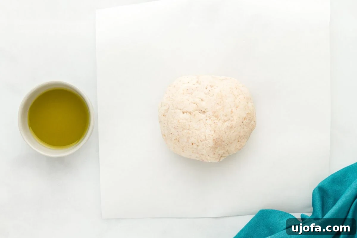 A ball of coconut flour tortilla dough resting on a piece of parchment paper, next to a small bowl of olive oil, ready to be divided.