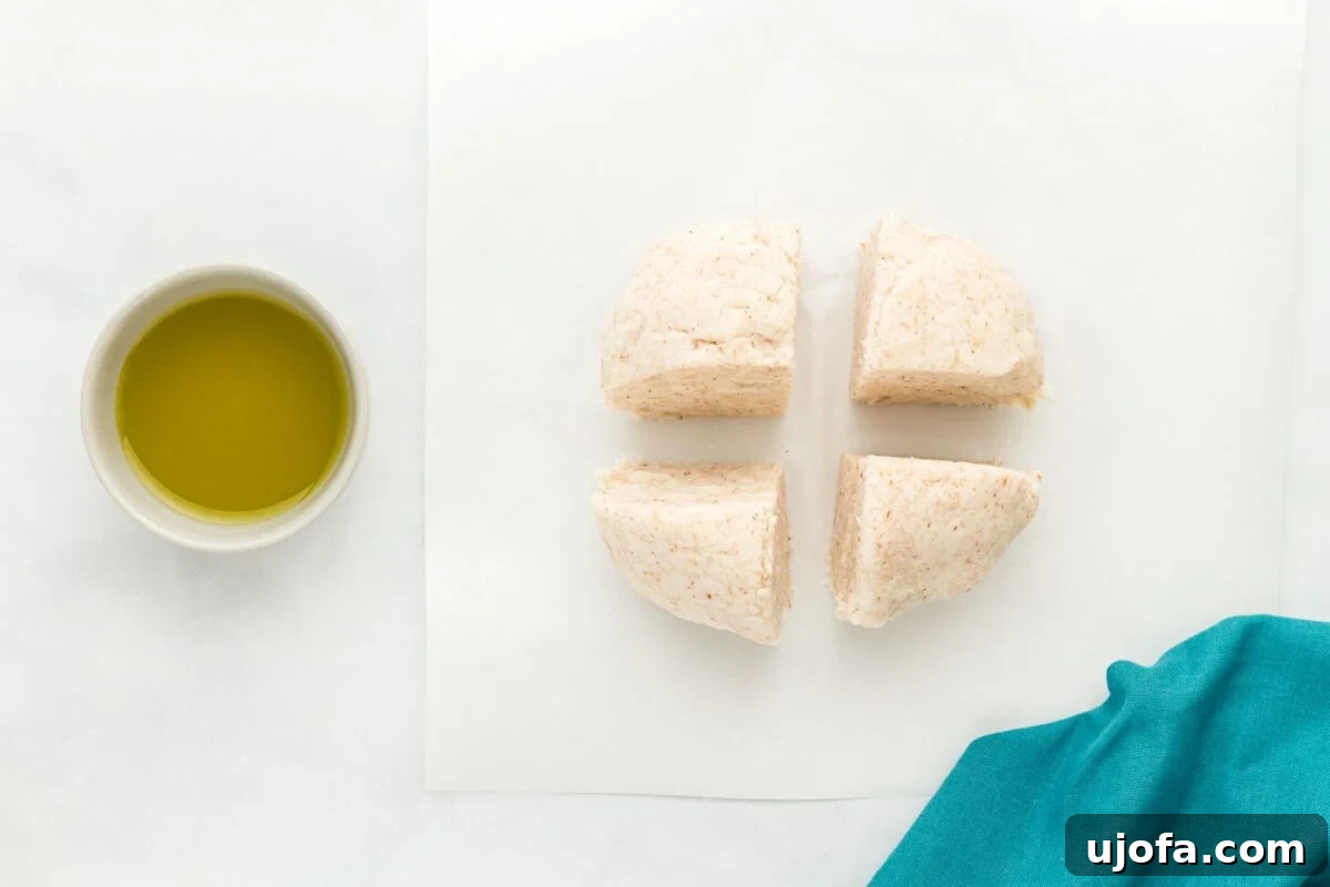 A ball of coconut flour tortilla dough divided into four equal quarters on parchment paper, with a bowl of olive oil nearby, illustrating the portioning step.