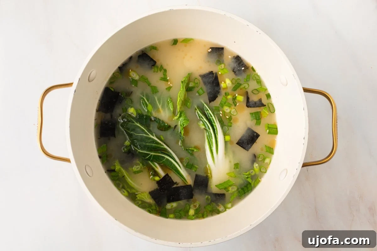 gluten-free miso soup cooking in a large pot with baby bok choy, green onions, and seaweed floating