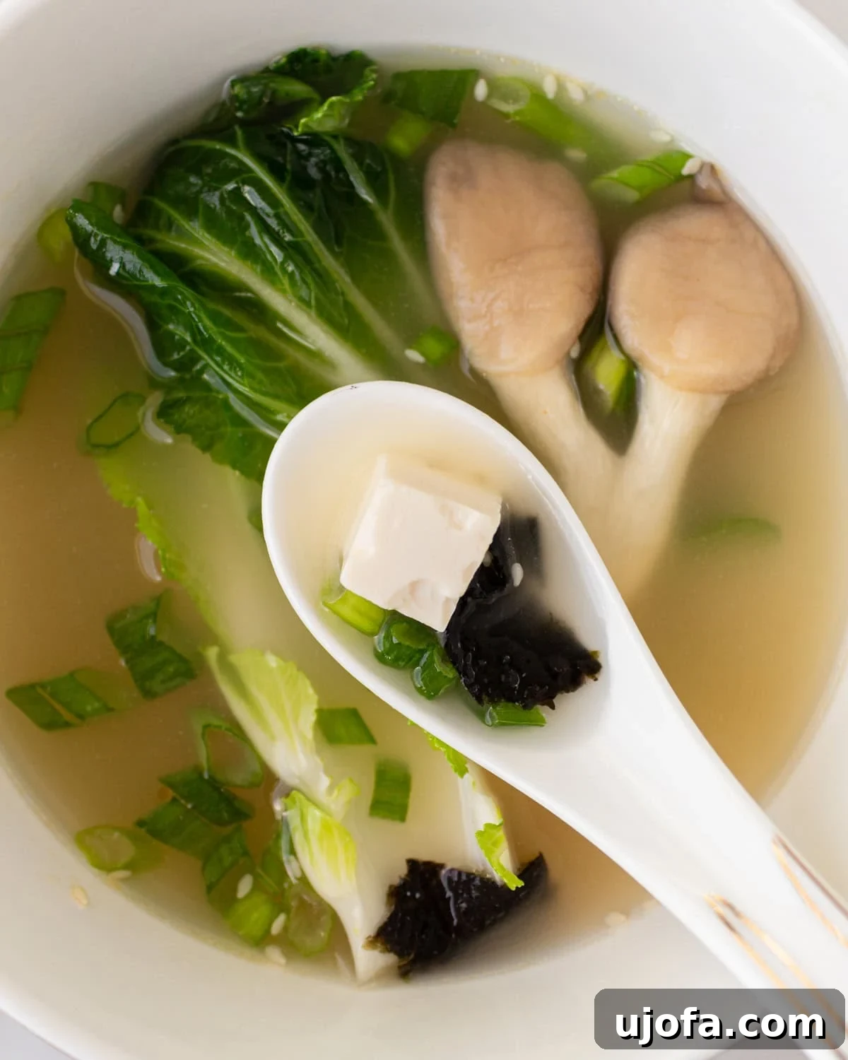 white soup spoon with a piece of tofu and seaweed hovering over bowl of gluten-free miso soup