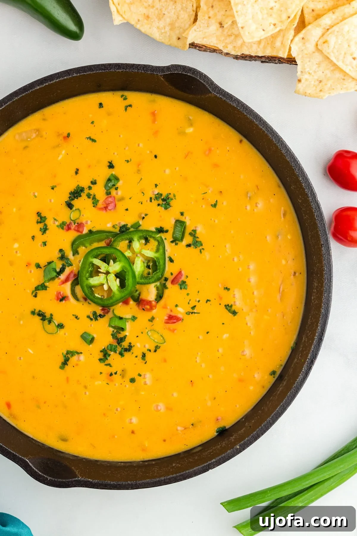 Creamy Vegan Queso 2 closeup of vegan queso in a black skillet topped with jalapenos and red peppers