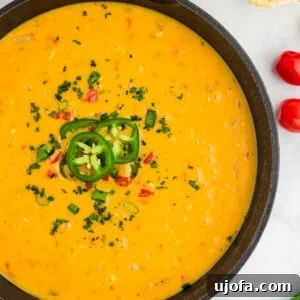 closeup of vegan queso in a black skillet topped with jalapenos and red peppers