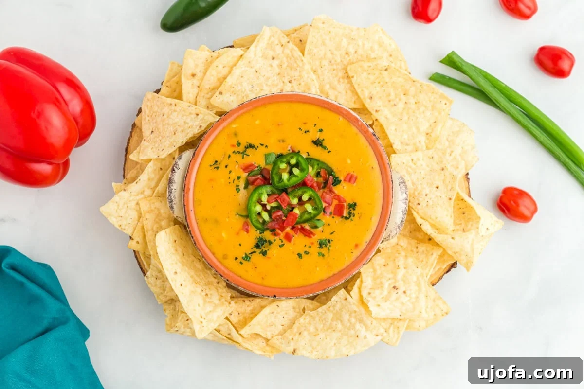 Creamy Vegan Queso 7 vegan queso in bowl topped with jalapenos, red peppers, and green onions surrounded by tortilla chips and red bell peppers