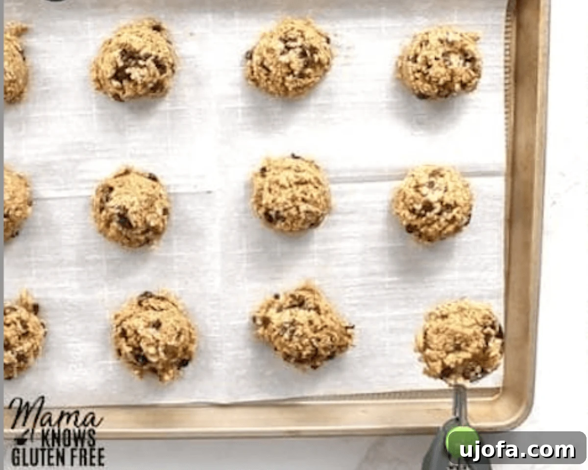A parchment-lined baking sheet with scoops of gluten-free breakfast cookie dough neatly arranged before baking. A cookie scoop is visible in the corner.