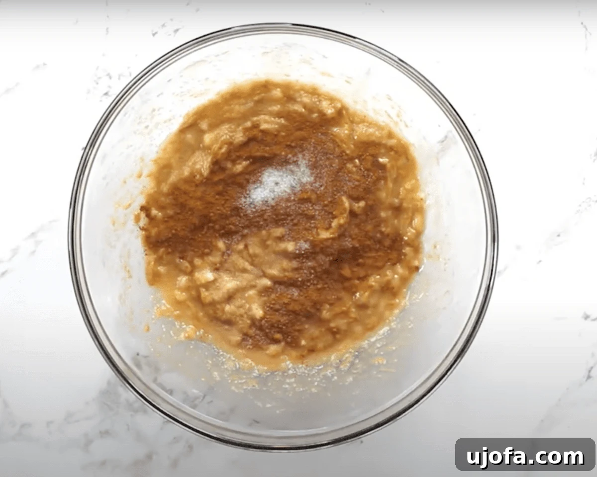 A glass bowl with mashed bananas, peanut butter, and honey, now topped with ground cinnamon and salt, ready to be stirred.