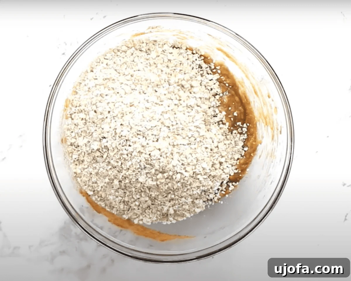 A mixing bowl showing gluten-free quick oats piled on top of the wet ingredients, before being mixed together.