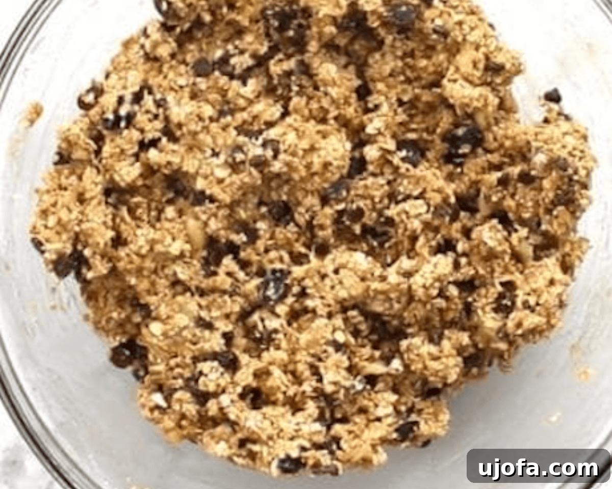 A glass bowl with fully mixed gluten-free breakfast cookie dough, packed with chocolate chips and raisins.