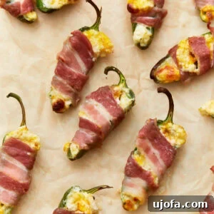 Close-up of bacon-wrapped keto jalapeño poppers stuffed with a creamy cheese mixture, placed on parchment paper, golden and crispy from baking.