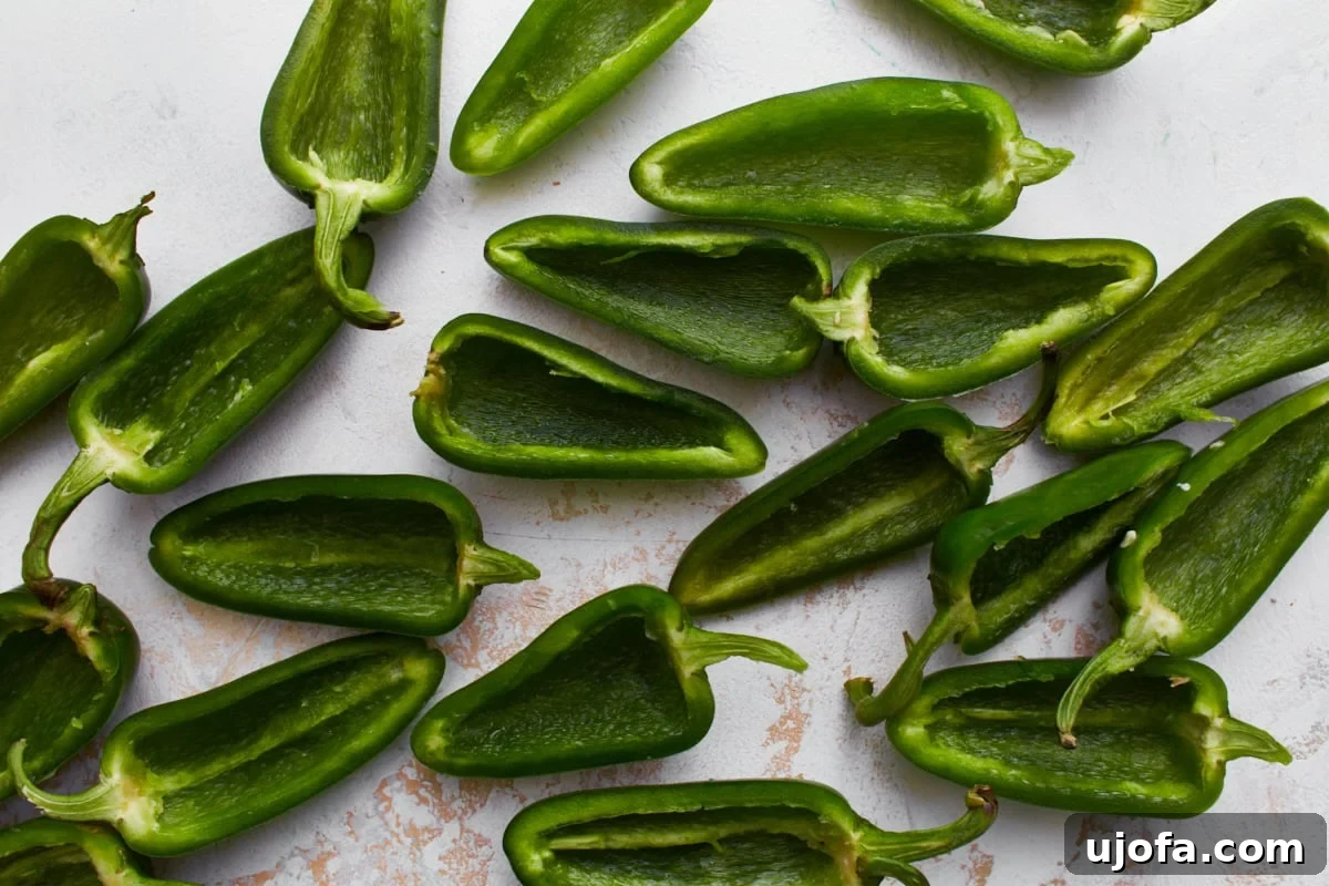 Fresh jalapeños, neatly sliced in half lengthwise with their membranes and seeds removed, laid out on a cutting board.