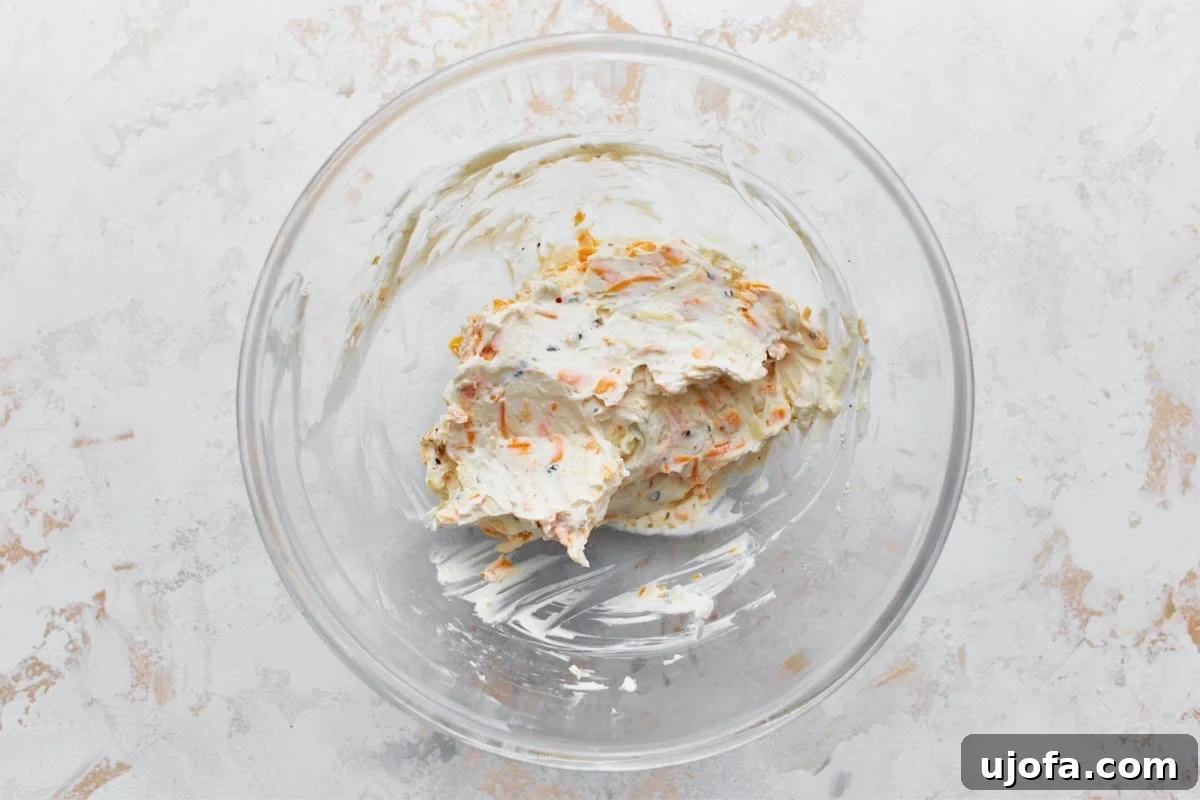 A glass mixing bowl filled with a creamy, rich mixture of softened cream cheese, shredded cheddar and mozzarella, and aromatic garlic and onion powder, ready to be combined.