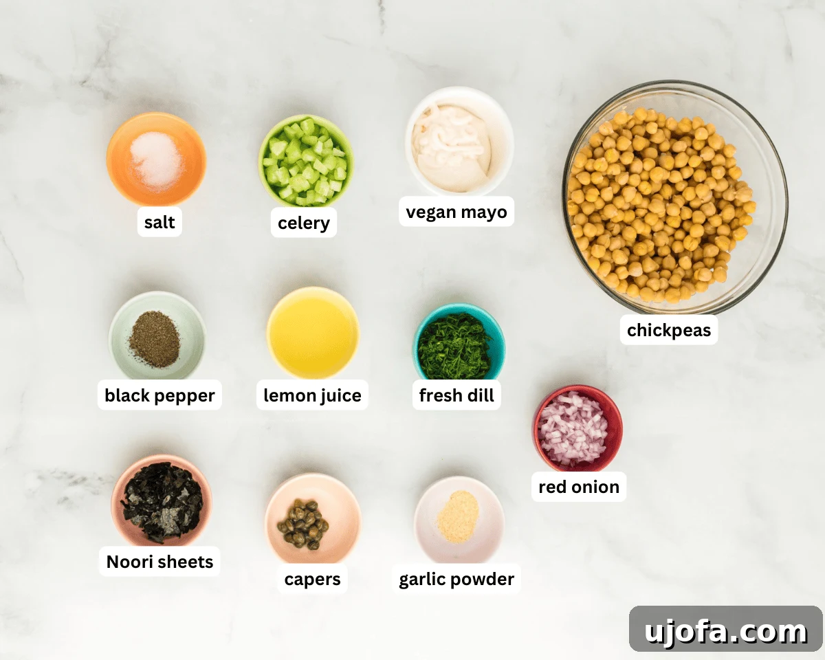 Vegan chickpea tuna salad ingredients laid out on a light surface, showcasing fresh vegetables, capers, chickpeas, and nori sheets.