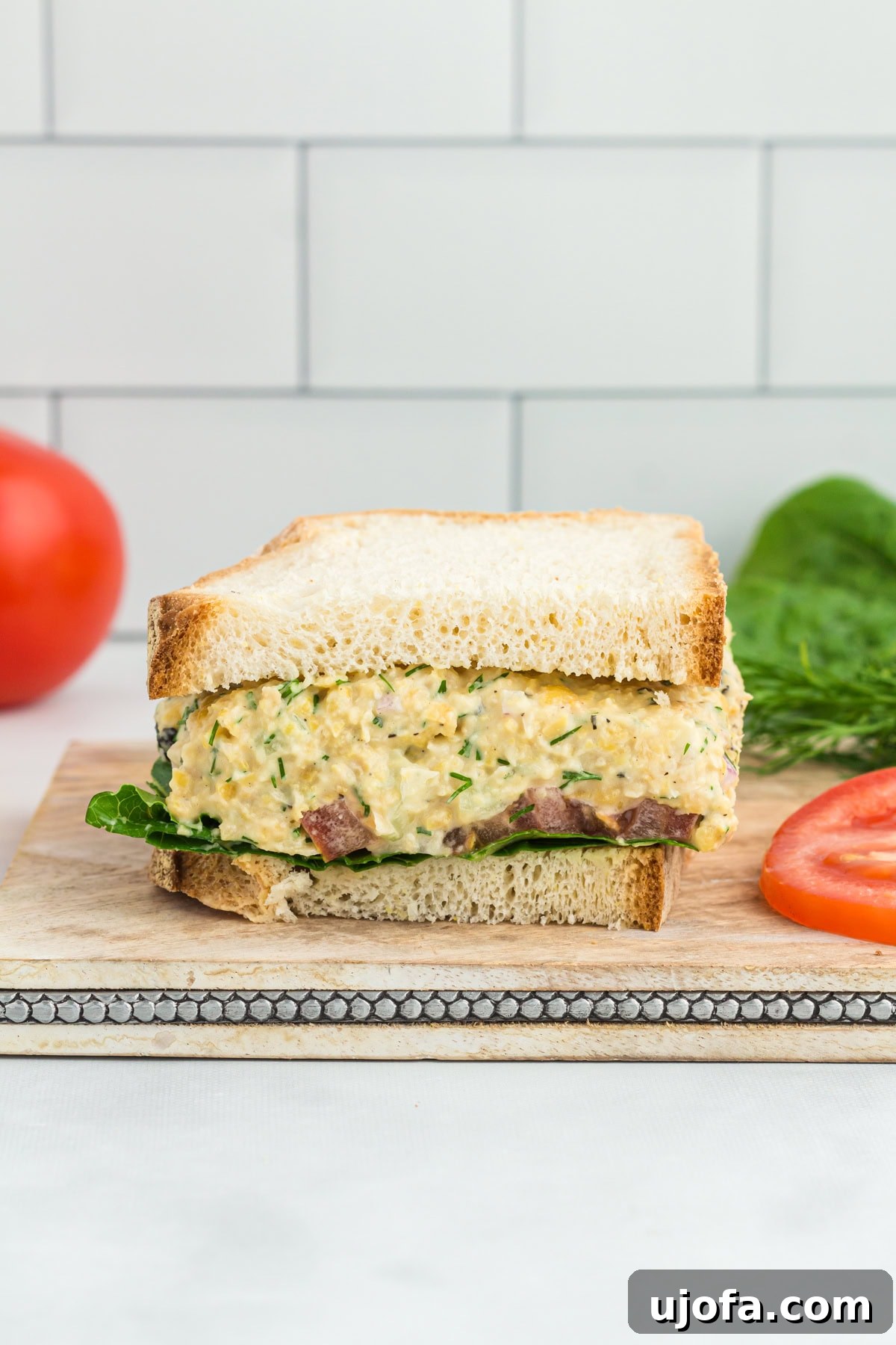 A sandwich made with vegan chickpea tuna salad, featuring creamy filling mixed with herbs and diced vegetables, layered on a slice of bread with fresh greens.