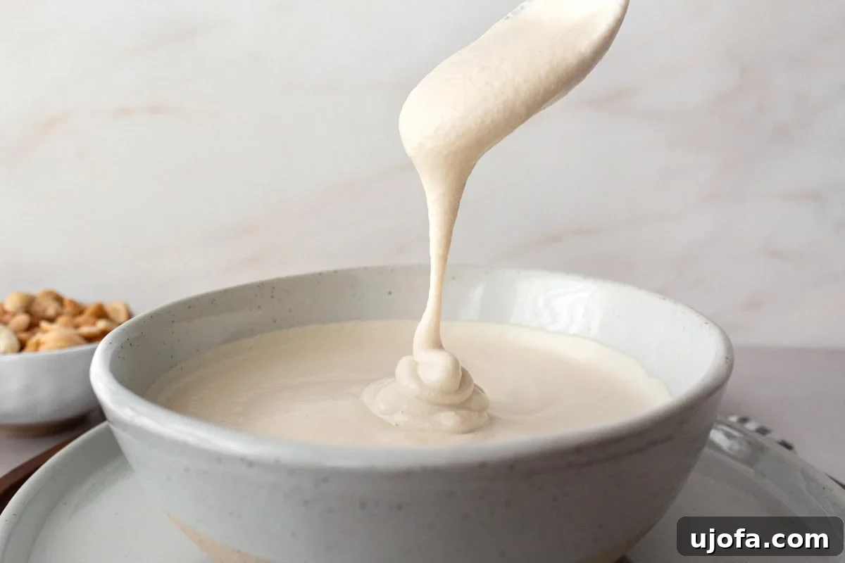 A spoon drizzling creamy cashew cream into a bowl, showing its smooth and thick texture