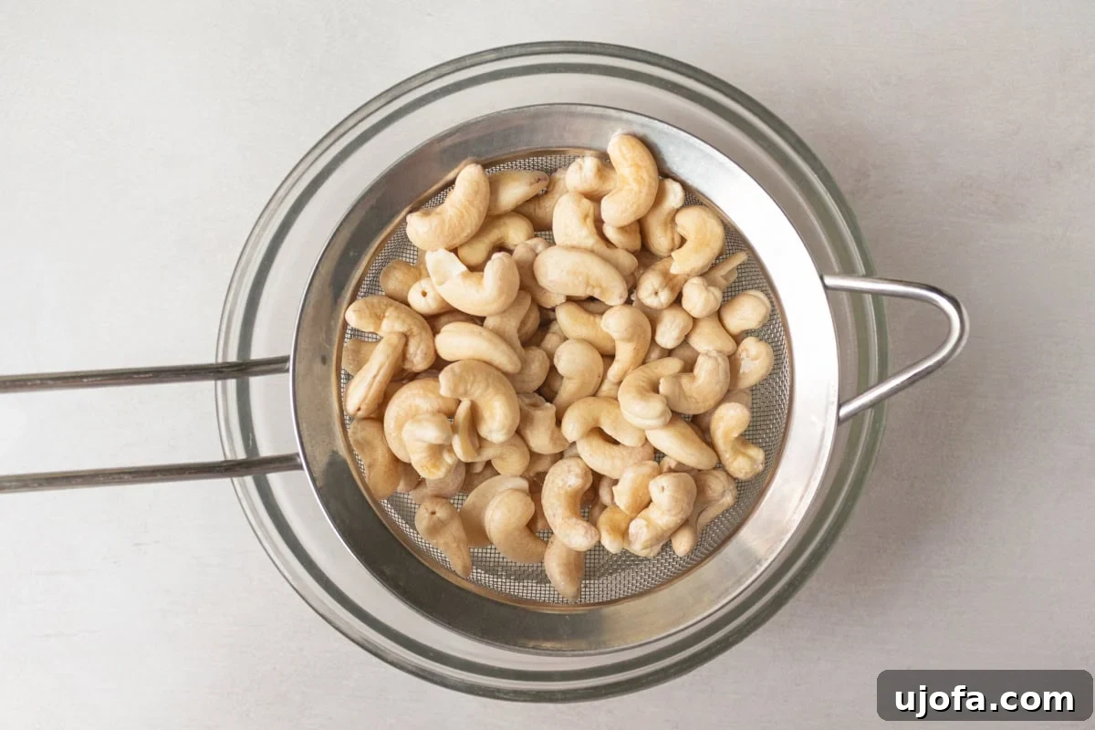 soaked raw cashews in a sieve draining over a glass bowl