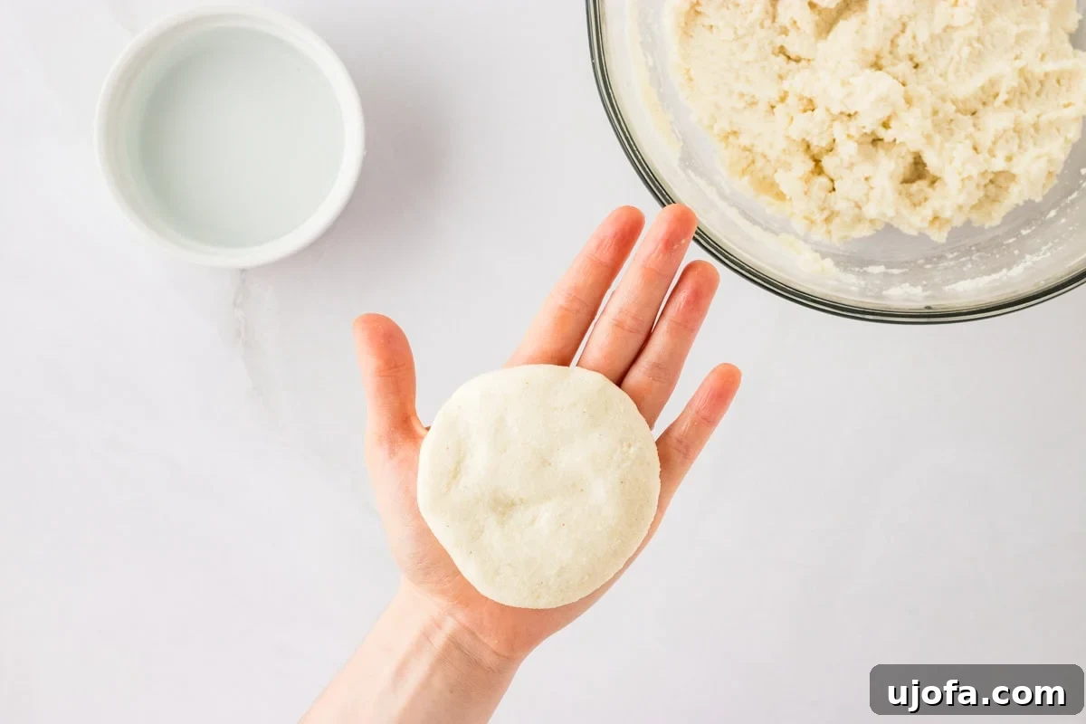 Crafting Perfect Arepas 9 A hand with smooth formed arepa dough resting in the palm. In the background the remaining dough is in a glass bowl next to a small ramekin with water.