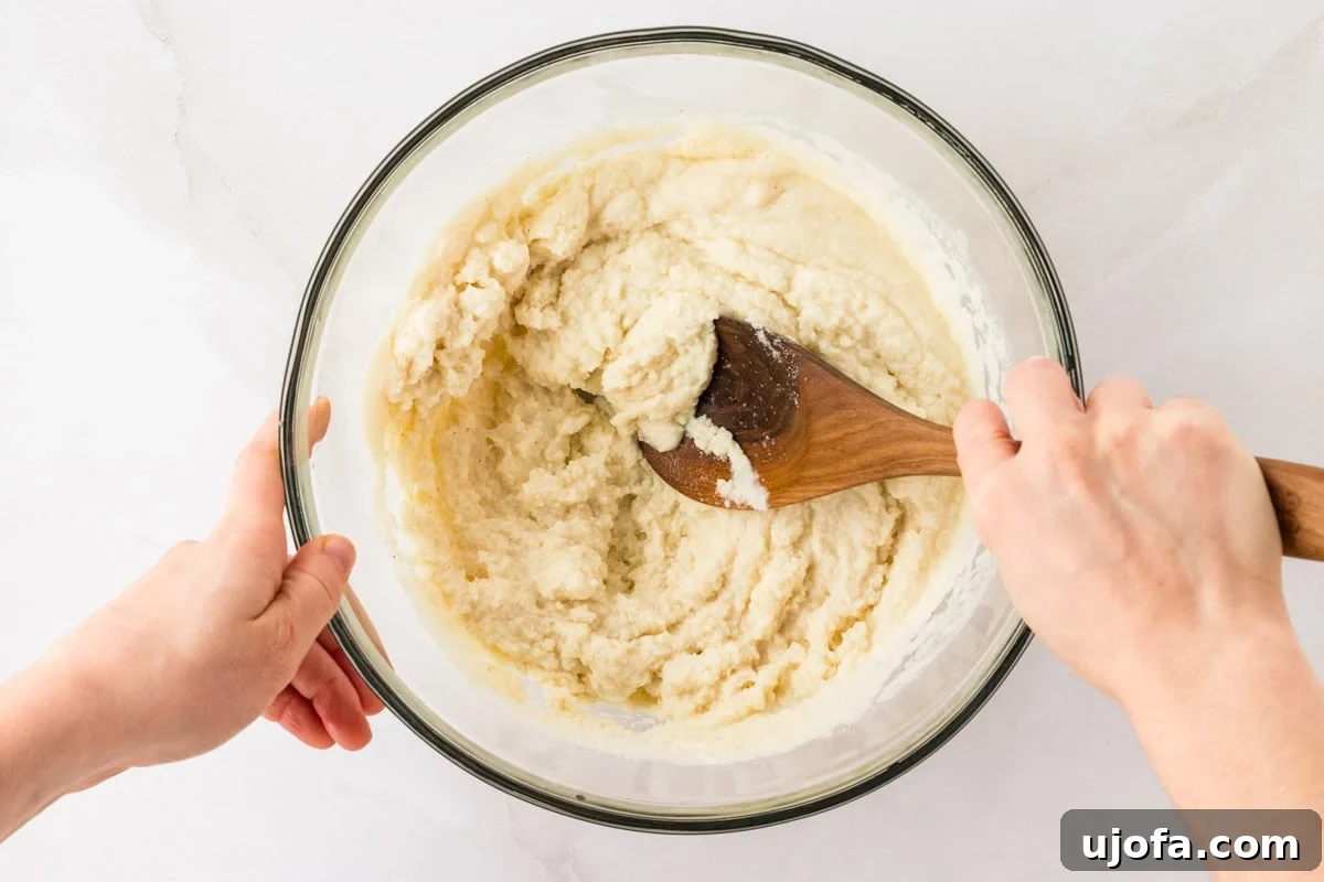 Crafting Perfect Arepas 6 Hands mixing arepa dough in a clear glass bowl with a wooden spoon. The dough has a smooth, slightly thick consistency, ready to be shaped into arepas.