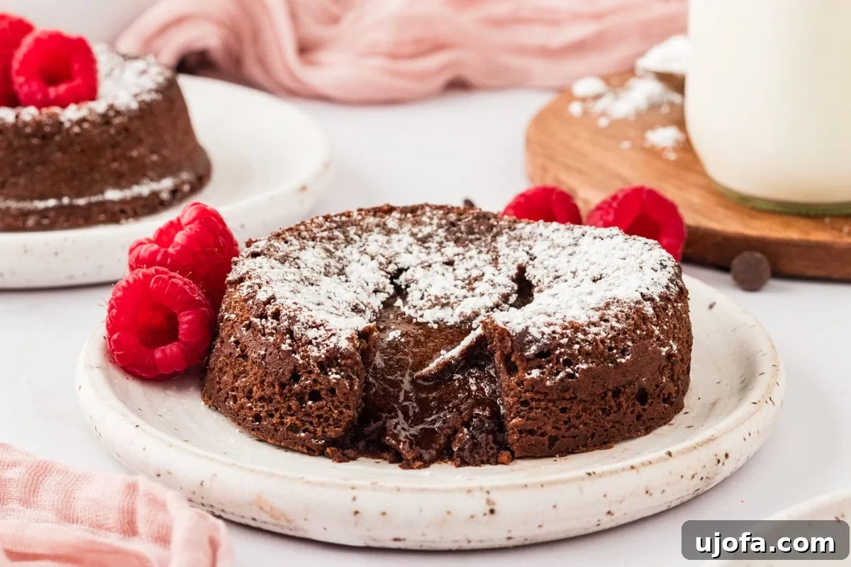Molten Gluten Free Chocolate Bliss 16 A gluten-free chocolate lava cake on a white plate, dusted with powdered sugar with a gooey chocolate center with raspberries resting on the plate.