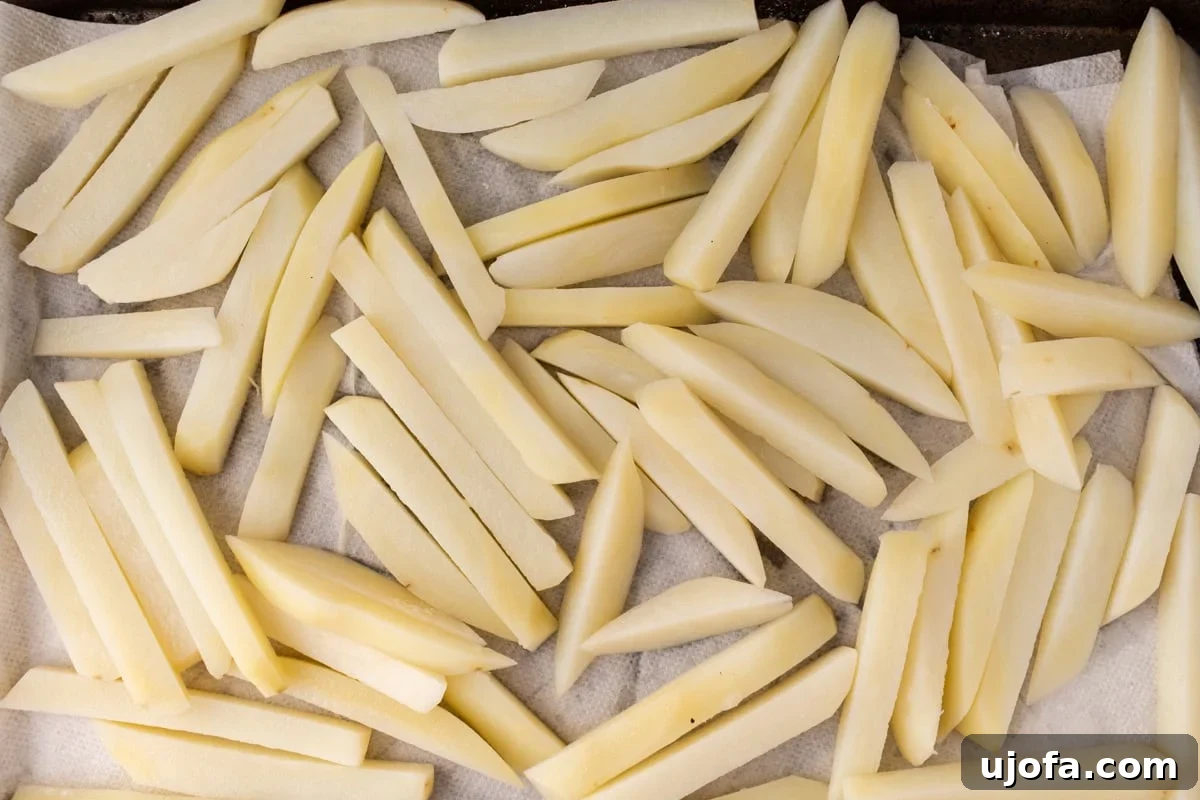 raw French fries on a parchment-lined baking sheet, freshly cut